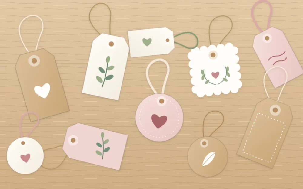 Handmade tags in kraft, ivory and blush cardstock scattered on a table, each with a punched hole and a loop of twine or ribbon