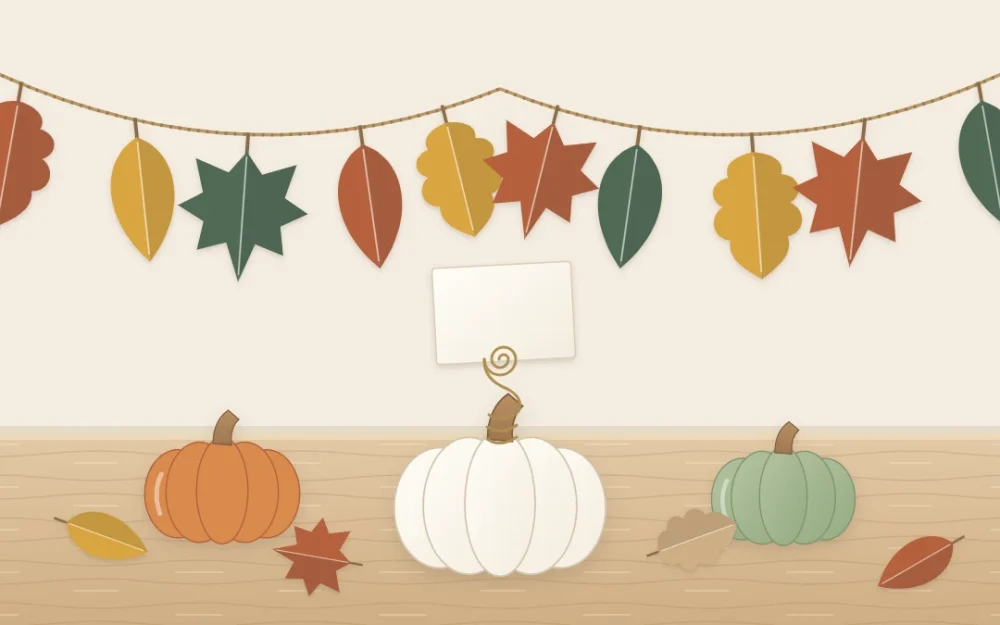 A garland of paper leaves in rust, mustard and deep green above three small pumpkins, one holding a blank card in a wire coil