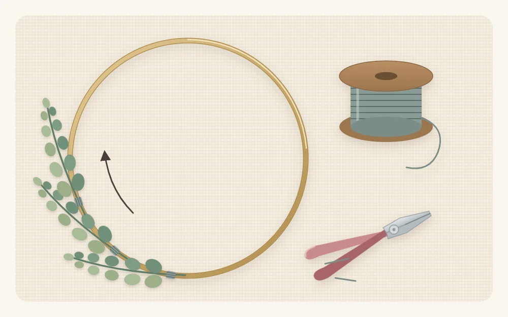 A bare metal hoop with three greenery sprigs wired on in one direction, beside floral wire and wire cutters