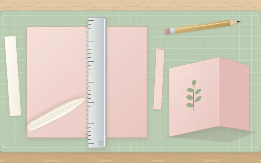 Blush cardstock on a sage cutting mat with a metal ruler along a scored line, a bone folder and a crisply folded card